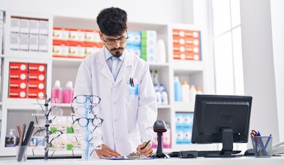 Wall Mural - Young hispanic man pharmacist writing on paper standing at pharmacy