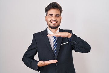 Poster - Young hispanic man with tattoos wearing business suit and tie gesturing with hands showing big and large size sign, measure symbol. smiling looking at the camera. measuring concept.