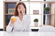 Brunette woman drinking glass of orange juice yawning tired covering half face, eye and mouth with hand. face hurts in pain.