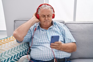 Poster - Middle age grey-haired man listening to music sitting on sofa at home