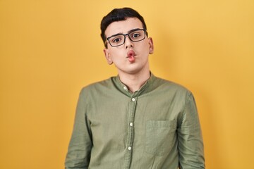 Poster - Non binary person standing over yellow background making fish face with lips, crazy and comical gesture. funny expression.