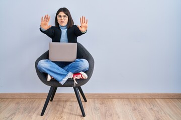 Sticker - Young hispanic woman sitting on chair using computer laptop doing stop gesture with hands palms, angry and frustration expression