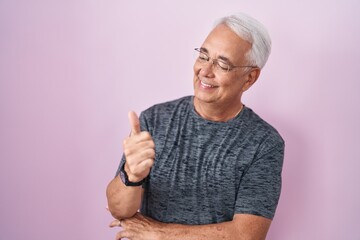 Poster - Middle age man with grey hair standing over pink background looking proud, smiling doing thumbs up gesture to the side