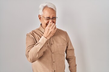 Sticker - Hispanic senior man wearing glasses smelling something stinky and disgusting, intolerable smell, holding breath with fingers on nose. bad smell