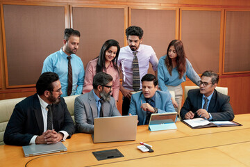 Indian businesspeople group working together and looking in laptop at meeting hall.