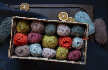 Colorful alpaca wool yarn skeins in a basket on a dark background, yarn balls flat lay top view