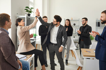 Happy colleagues man and woman giving high five at meeting at the office, celebrating success, making a deal or business achievement. Coworkers applaud congratulating their partners on job well done.