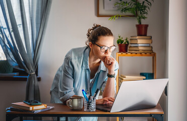 Wall Mural - Young female freelancer working learning from home at home using laptop with chart on screen. Remote work and online education concept