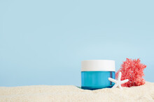 Cosmetic Cream In Blue Glass Bottle With Starfish And Pink Seaweed On The Sand On Blue Background, Copy Space. UVA And UVB Protection. Summer Cosmetics