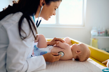 Wall Mural - Happy pediatrician using stethoscope while listening baby's lungs during medical appointment.