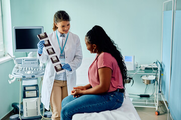 Wall Mural - Happy doctor showing sonogram to black female patient after ultrasound examination at clinic.