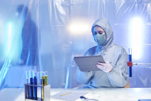 Female Scientist Wearing Full Protective Suit Working At Desk In Biohazard Dange Zone, Copy Space