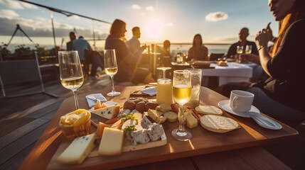 People eating cheese and drinking wine at rooftop restaurant at sunset time