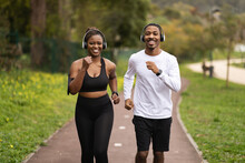 Positive Young Black Couple In Wireless Headphones Listen Music, Run In Summer Park