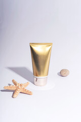 Wall Mural - Golden cream tube and starfish on white background with hard shadows. Sunscreen, natural cosmetics concept. Closeup