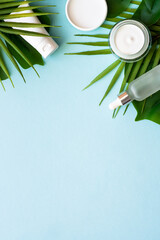 Wall Mural - natural cosmetic products. cream, serum, tonic with green tropical leaves. flat lay on blue backgrou