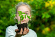 © Petr Bonek - Young teenage girl holds a tomato sprout in her outstretched hands. Women's hands carefully stretch out a young tomato sprout. Spring planting vegetables in the garden.