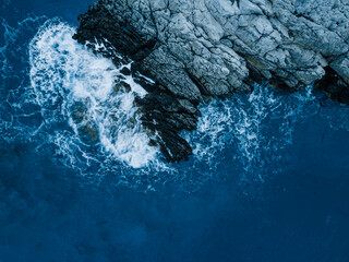 Drone above of turquoise ocean waves crashing and white foaming on huge reef rock stones. Wild sea washing reef rock cliff