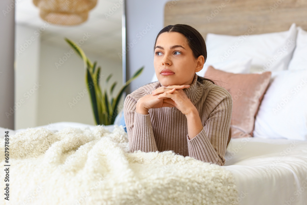 Thoughtful young woman lying on bed at home