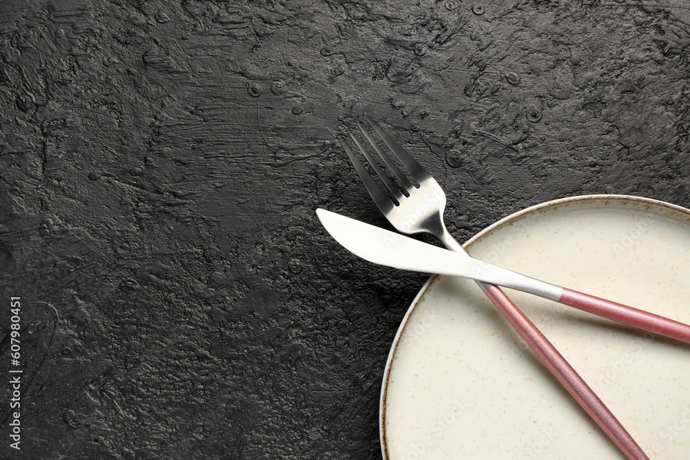 Plate with stainless steel fork and knife on black background