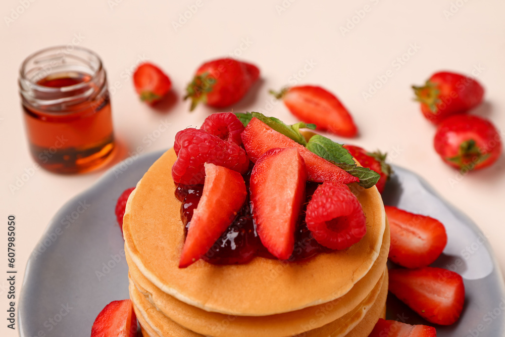 Plate with sweet pancakes, berries and jam on beige background, closeup