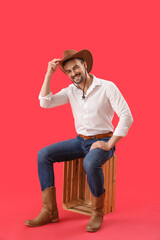 Wall Mural - Handsome cowboy sitting on red background