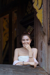 A pretty Asian girl wearing a traditional Thai dress in the countryside sits happily by the window of a beautiful ancient house in Chiang Mai the Northern of Thailand.