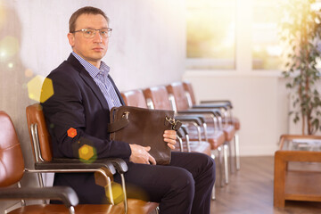 Wall Mural - Adult man in business suit and glasses sits in line on chair in reception