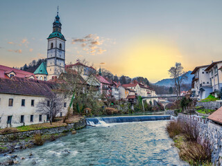 Wall Mural - Skofja Loka village houses on Selca Sora river and Kapucinski samostan church tower during sunset, Slovenia