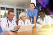 © JackF - In morning meeting, doctors of emergency department confer about patients clinical case. Male health worker with colleagues sitting at table, reading new article on laptop and discussing information