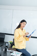 © ND STOCK - Portrait of young asian woman in casual wear holding clipboard, while standing in modern office room.