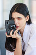 © Bangkok Click Studio - Closeup shot of Millennial Asian beautiful confident female model in white clean bathrobe sitting smiling posing holding mirrorless DSLR camera ready for work with photographer in photography studio