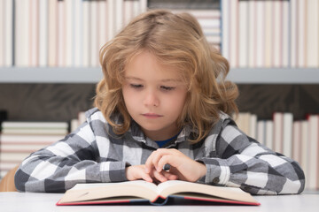 Portrait of school boy reading book in library. Kids development, learn to read. Child boy sitting in a book store, reading books.