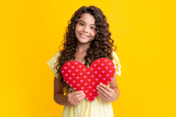 Happy teenager portrait. Lovely romantic teenage girl hold red heart symbol of love for valentines day isolated on yellow background. Smiling girl.