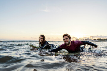 Wall Mural - Happy couple of surfers swimming with boards in water.