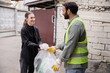 © LIGHTFIELD STUDIOS - Smiling young volunteer giving plastic bag with trash to indian worker in protective vest and gloves outdoors in waste disposal station, garbage sorting and recycling concept
