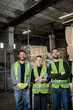 © LIGHTFIELD STUDIOS - Smiling interracial sorters in protective vests holding digital tablet and looking at camera near waste paper in waste disposal station, garbage sorting and recycling concept