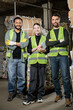 © LIGHTFIELD STUDIOS - Positive worker in protective vest holding digital tablet and standing near multiethnic colleagues and waste paper in waste disposal station, garbage sorting and recycling concept