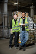 © LIGHTFIELD STUDIOS - Positive young sorter in protective vest and gloves looking at camera while standing near indian colleague and blurred waste paper in waste disposal station, garbage sorting and recycling concept