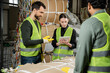 © LIGHTFIELD STUDIOS - Young worker in protective vest and gloves using digital tablet near smiling multiethnic colleagues and waste paper in garbage sorting center, waste sorting and recycling concept