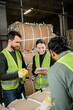 © LIGHTFIELD STUDIOS - Cheerful young woman in safety vest using digital tablet near multiethnic colleagues while working with waste paper in garbage sorting center, waste sorting and recycling concept