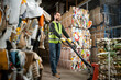 © LIGHTFIELD STUDIOS - Bearded sorter in protective gloves and vest moving waste paper on hand pallet truck in blurred garbage sorting center, waste sorting and recycling concept