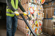 © LIGHTFIELD STUDIOS - Cropped view of male sorter in protective gloves and vest using hand pallet truck while working near waste paper in blurred garbage sorting center, waste sorting and recycling concept