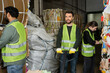 © LIGHTFIELD STUDIOS - Smiling worker in protective vest and gloves standing near hand pallet truck and next to multiethnic colleagues working with waste paper in garbage sorting center, waste sorting and recycling concept