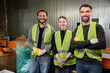 © LIGHTFIELD STUDIOS - Positive interracial workers in high visibility vests and gloves looking at camera while standing near conveyor and working in waste disposal station, recycling concept