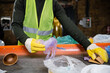 © LIGHTFIELD STUDIOS - Cropped view of sorter in protective gloves and vest taking garbage from conveyor while working in blurred garbage sorting center, garbage sorting and recycling concept