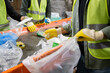 © LIGHTFIELD STUDIOS - Cropped view of sorter in gloves and protective vest holding blurred plastic bag and taking trash from conveyor while working near colleagues in waste disposal station, garbage recycling concept