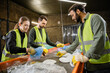 © LIGHTFIELD STUDIOS - Multiethnic workers in protective vests and gloves taking trash from conveyor while working together in waste disposal station at background, garbage sorting and recycling concept