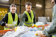 © LIGHTFIELD STUDIOS - Male worker in protective vest taking plastic from conveyor while working near interracial colleagues in blurred garbage sorting center, garbage sorting and recycling concept