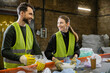 © LIGHTFIELD STUDIOS - Cheerful young worker in gloves and protective vest talking to colleague while taking garbage from conveyor and working in waste disposal station, garbage sorting and recycling concept